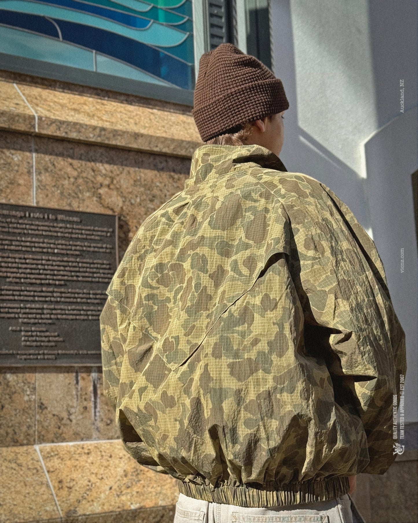 Bence in Waffle Beanie and VIC duck Camo Windbreaker. Created in a lightweight, water repellent polyester fabric that dries fast and provides protection from wind and rain showers. Mesh lined for breathability, the windbreaker features our feather logo on the left chest, 2 side pockets with zip closure, back cape vents for improved airflow and moisture control and a relaxed boxy fit.